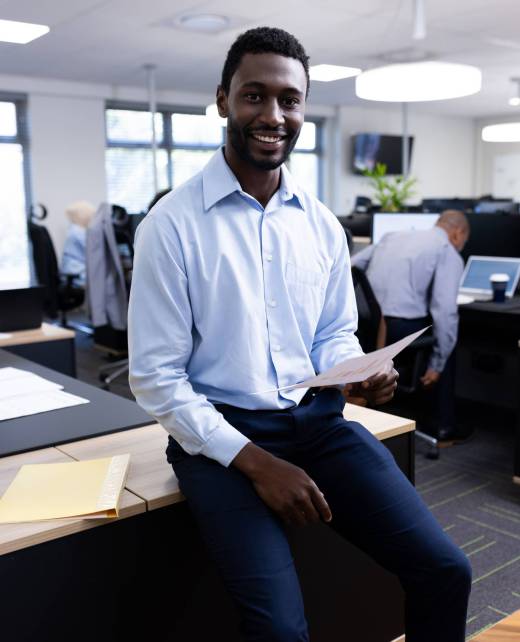 Vertical image of happy african american businessman looking at camera in office. Business professionals, job, corporation and working in office concept.